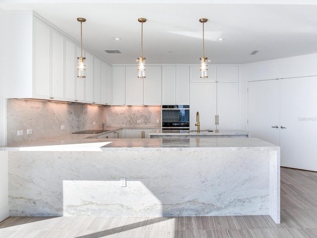 kitchen featuring light stone counters, light hardwood / wood-style flooring, pendant lighting, black electric cooktop, and white cabinets