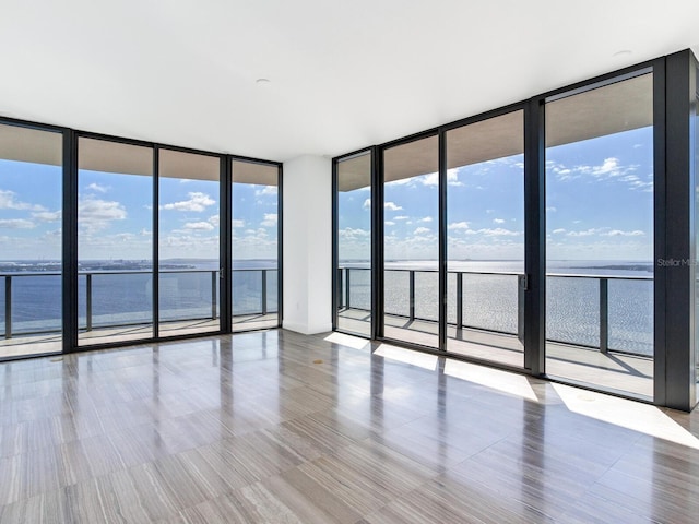 unfurnished room featuring light hardwood / wood-style flooring, a water view, and floor to ceiling windows