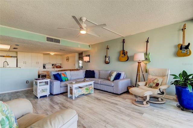 living room with a textured ceiling, light hardwood / wood-style floors, and ceiling fan