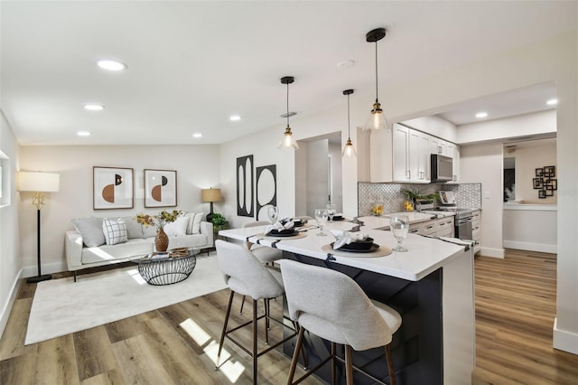 kitchen with stainless steel electric range oven, white cabinets, decorative light fixtures, light wood-type flooring, and a kitchen bar