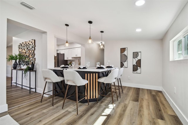 kitchen featuring white cabinetry, kitchen peninsula, decorative light fixtures, fridge, and a breakfast bar area