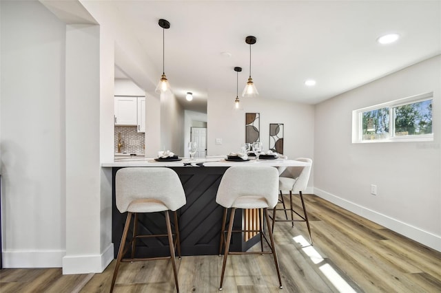 kitchen with decorative backsplash, decorative light fixtures, light wood-type flooring, white cabinetry, and kitchen peninsula