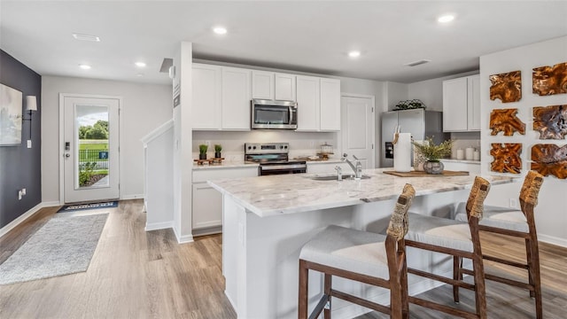 kitchen with light stone countertops, light hardwood / wood-style floors, a center island with sink, white cabinets, and appliances with stainless steel finishes