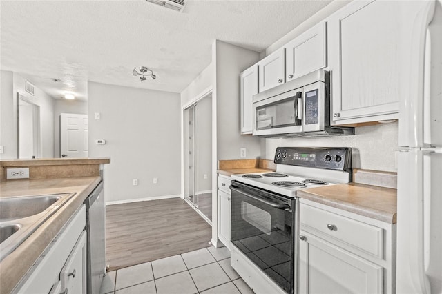 kitchen featuring white cabinets, sink, light tile patterned floors, a textured ceiling, and appliances with stainless steel finishes