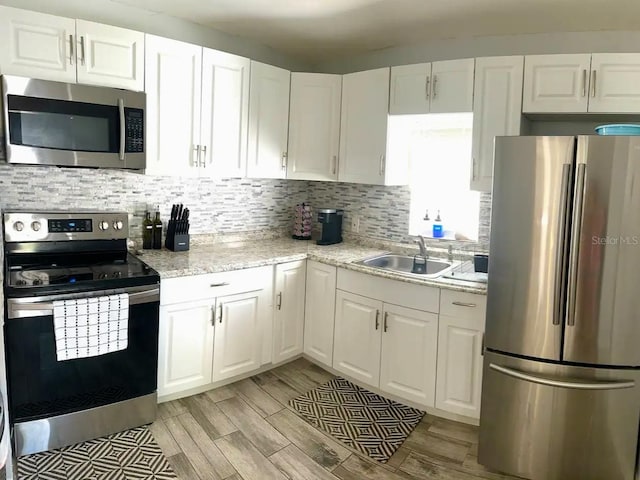 kitchen featuring light stone countertops, sink, appliances with stainless steel finishes, white cabinets, and light wood-type flooring