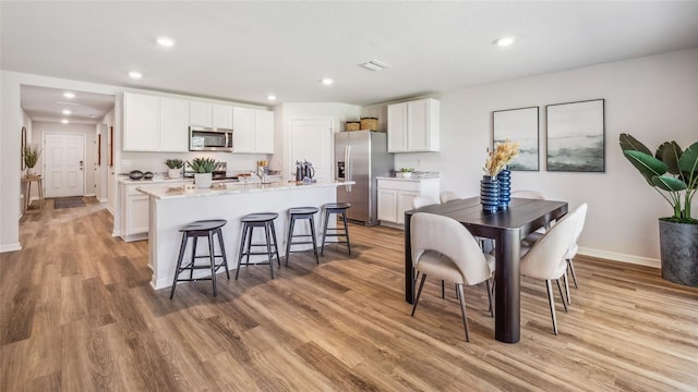 kitchen with an island with sink, light hardwood / wood-style floors, a breakfast bar, white cabinets, and appliances with stainless steel finishes