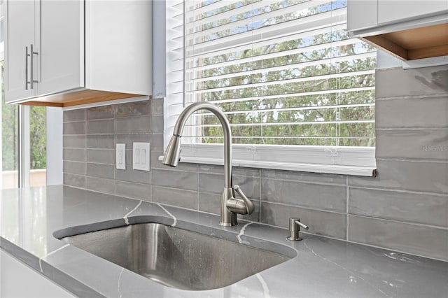 interior details with decorative backsplash, light stone countertops, white cabinetry, and sink