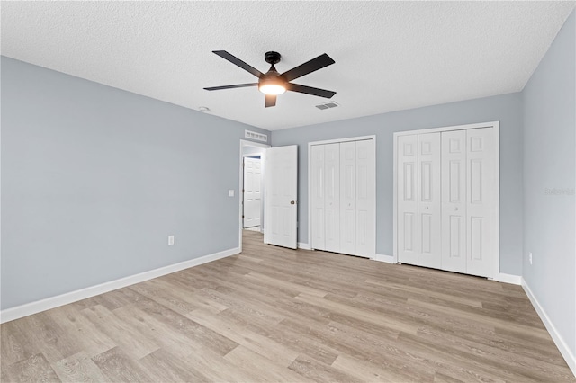 unfurnished bedroom featuring a textured ceiling, two closets, light hardwood / wood-style flooring, and ceiling fan