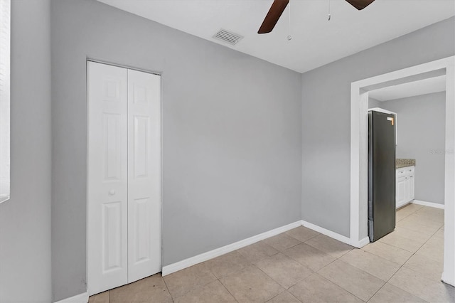 unfurnished bedroom featuring stainless steel fridge, ceiling fan, light tile patterned flooring, and a closet