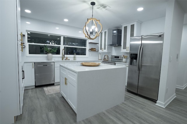 kitchen with wall chimney range hood, sink, decorative light fixtures, white cabinetry, and stainless steel appliances