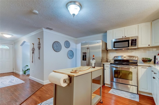 kitchen featuring white cabinetry, crown molding, a textured ceiling, appliances with stainless steel finishes, and light wood-type flooring