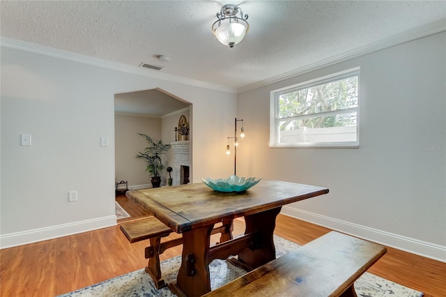 dining space with a brick fireplace, ornamental molding, a textured ceiling, and light hardwood / wood-style flooring