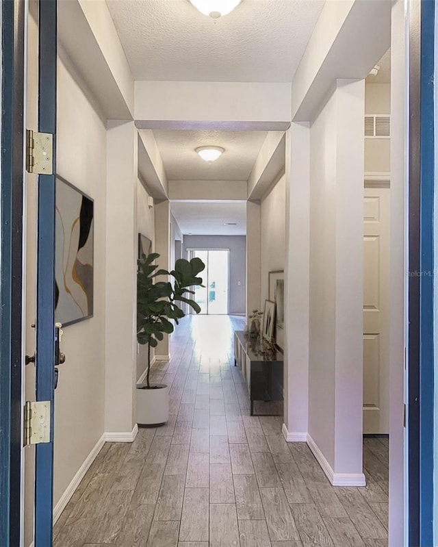 hall featuring light wood-type flooring and a textured ceiling