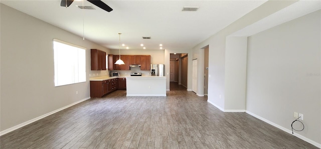 kitchen with pendant lighting, ceiling fan, appliances with stainless steel finishes, a kitchen island, and dark hardwood / wood-style flooring