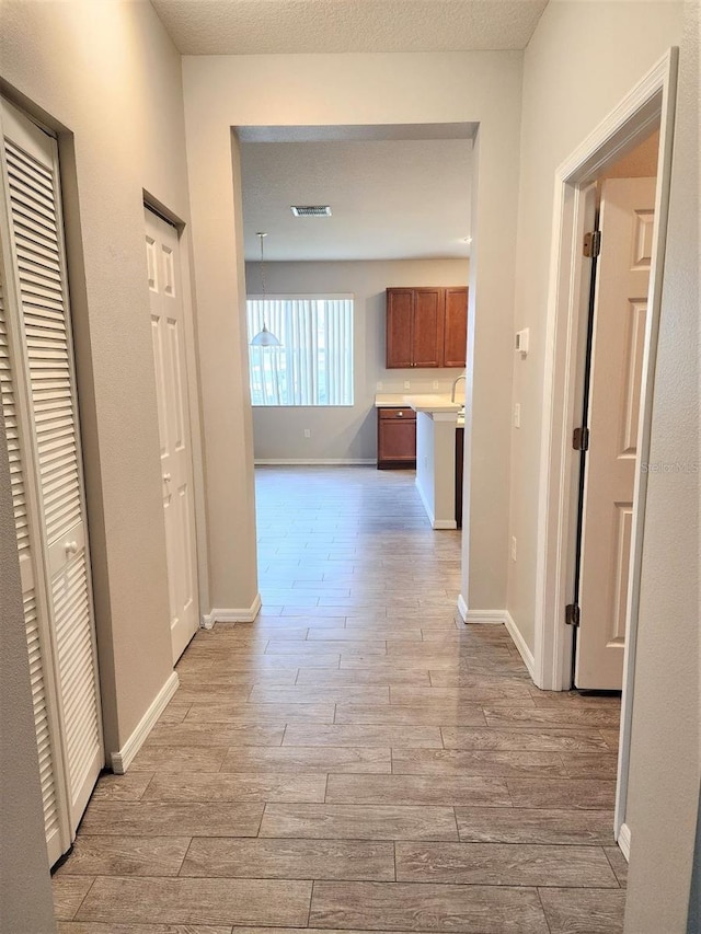 corridor with a textured ceiling and light hardwood / wood-style flooring