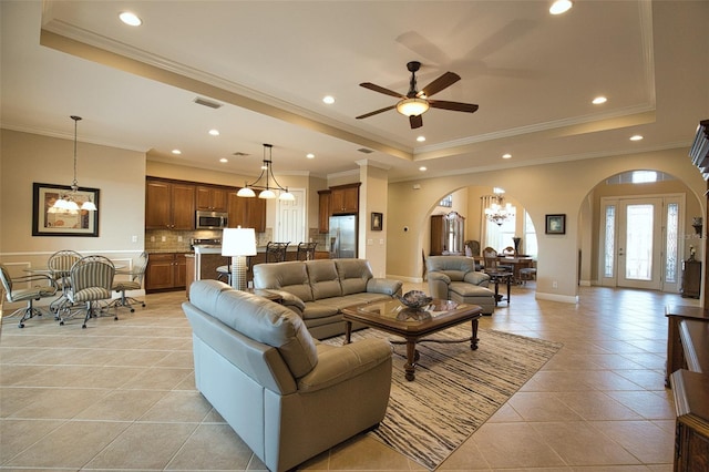 living room with crown molding, a tray ceiling, ceiling fan with notable chandelier, and light tile patterned floors