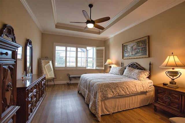 bedroom featuring dark wood-type flooring, ceiling fan, a tray ceiling, and crown molding