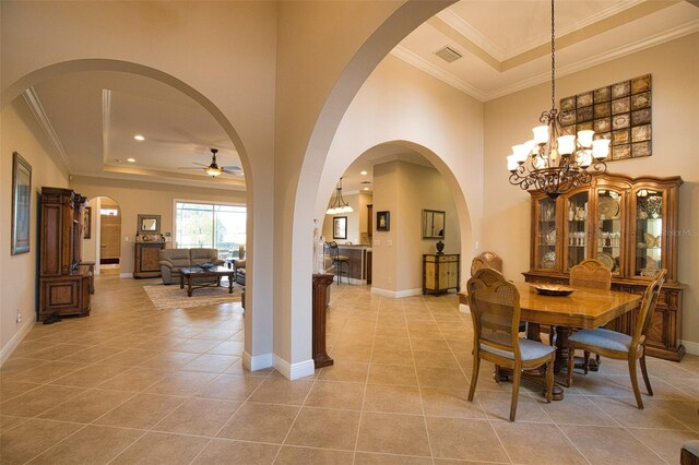 tiled dining room featuring crown molding, a tray ceiling, ceiling fan with notable chandelier, and a high ceiling