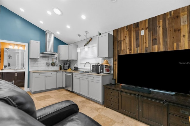 kitchen with wall chimney range hood, stainless steel dishwasher, vaulted ceiling, decorative light fixtures, and white cabinets