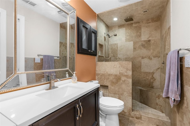 bathroom featuring vanity, toilet, tiled shower, and tile walls