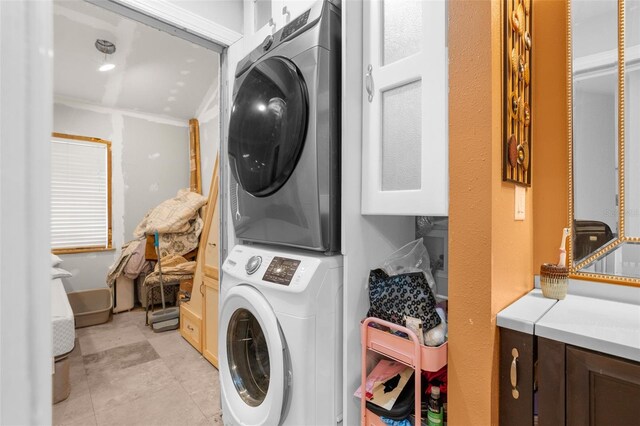 clothes washing area featuring crown molding, cabinets, and stacked washer and clothes dryer