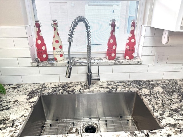 interior details featuring backsplash, white cabinetry, and sink