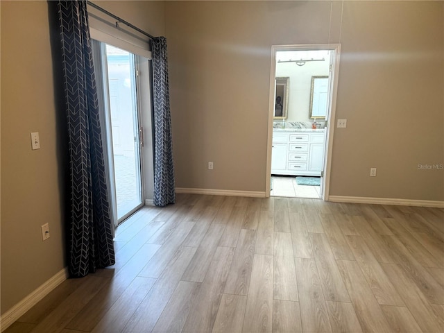 unfurnished bedroom featuring ensuite bath and light hardwood / wood-style floors