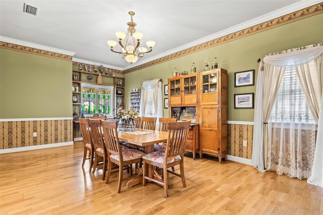 dining space featuring a notable chandelier, wood walls, ornamental molding, and light hardwood / wood-style flooring