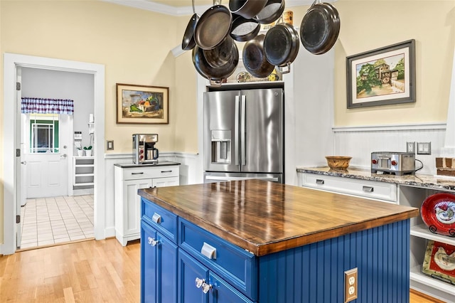 kitchen with wood counters, blue cabinets, white cabinetry, stainless steel fridge, and a center island