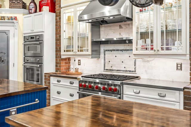 kitchen with butcher block counters, extractor fan, white cabinetry, appliances with stainless steel finishes, and backsplash