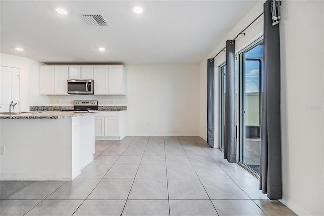 kitchen featuring white cabinets, light tile patterned flooring, light stone counters, and appliances with stainless steel finishes