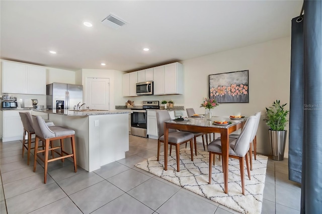 kitchen with a breakfast bar, a center island with sink, white cabinets, light stone counters, and stainless steel appliances