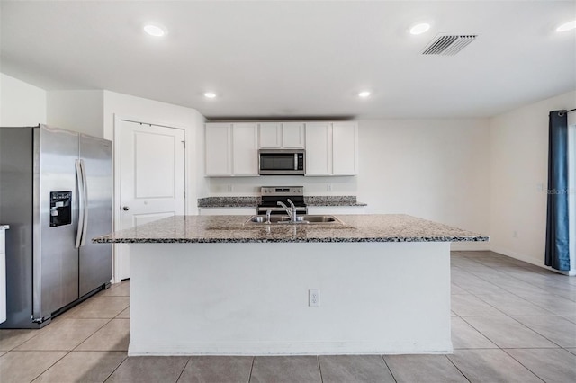 kitchen with appliances with stainless steel finishes, sink, stone countertops, white cabinets, and an island with sink