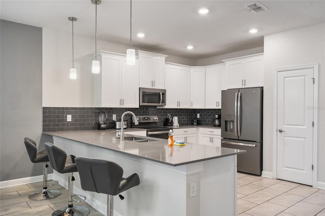 kitchen featuring white cabinets, kitchen peninsula, pendant lighting, light tile patterned flooring, and appliances with stainless steel finishes