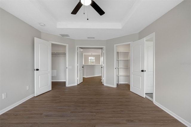 unfurnished bedroom featuring a raised ceiling, ceiling fan, dark hardwood / wood-style flooring, and a spacious closet