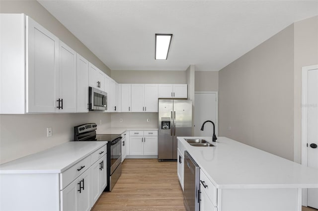 kitchen with light wood finished floors, light countertops, appliances with stainless steel finishes, a kitchen island with sink, and white cabinetry