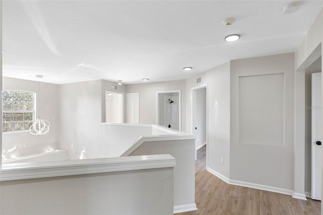 corridor featuring baseboards, visible vents, an upstairs landing, and light wood-style floors