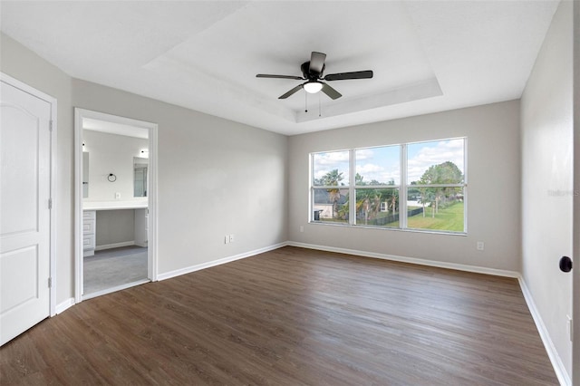 interior space with dark wood-style flooring, a raised ceiling, a ceiling fan, and baseboards