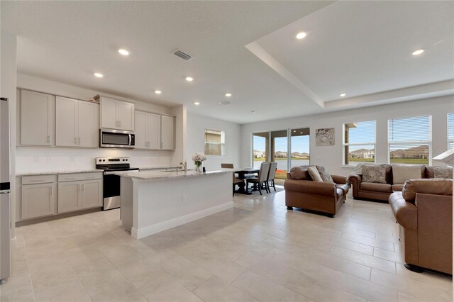 kitchen with light stone counters, a center island with sink, light tile patterned floors, and stainless steel appliances