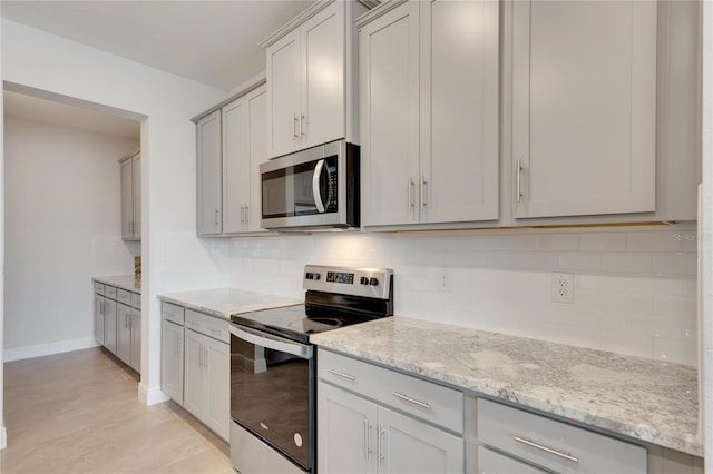 kitchen with light stone countertops, stainless steel appliances, light tile patterned floors, and tasteful backsplash