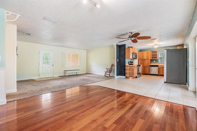 unfurnished living room with ceiling fan, light hardwood / wood-style floors, and a textured ceiling