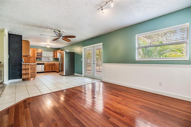 unfurnished living room featuring french doors, light wood-type flooring, a textured ceiling, and ceiling fan