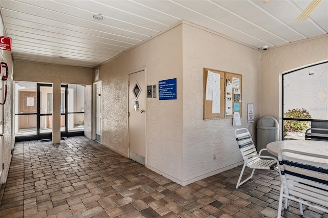 hallway featuring a textured wall and brick floor