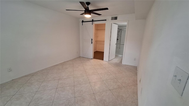 unfurnished bedroom with visible vents, a walk in closet, ceiling fan, a barn door, and light tile patterned floors