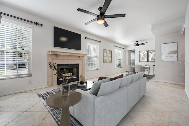 living area featuring a tiled fireplace, light tile patterned flooring, a ceiling fan, and baseboards