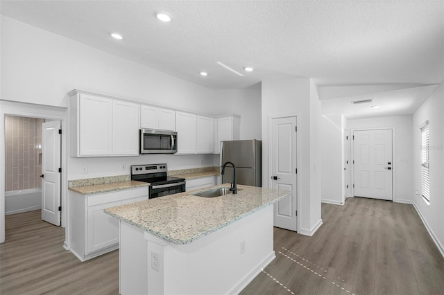 kitchen with appliances with stainless steel finishes, light wood-type flooring, sink, white cabinetry, and an island with sink