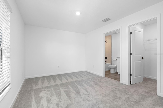 unfurnished bedroom with a walk in closet, light colored carpet, a closet, and ensuite bathroom