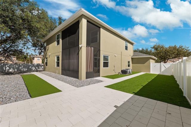 rear view of property with a sunroom, central air condition unit, a patio, and a lawn