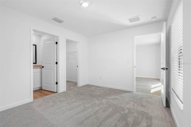 unfurnished bedroom featuring a walk in closet, light colored carpet, and multiple windows