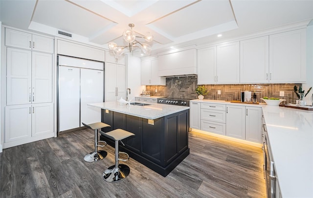 kitchen featuring paneled refrigerator, tasteful backsplash, a kitchen bar, a center island with sink, and custom range hood